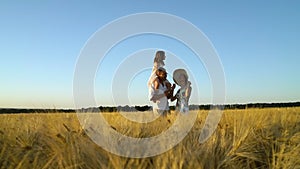 Happy parents and little daughter dancing in wheat field at sunset