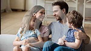 Happy parents with little daughter and son sitting on couch