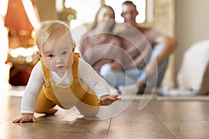 Happy Parents Looking At Adorable Infant Baby Crawling On Floor At Home