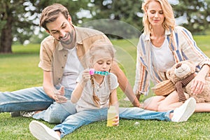 happy parents looking at cute little daughter blowing soap bubbles