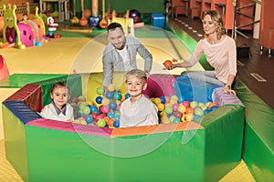 happy parents looking at cute little kids smiling at camera while sitting in pool