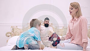 Happy parents playing with their son on the bed. her father and child son play in bedroom.