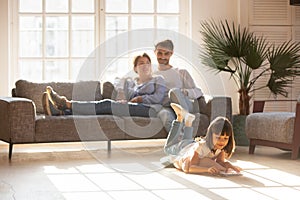 Happy parents relaxing on couch while kid drawing on floor