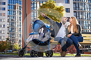 Happy parents sitting on bench with stroller in city.