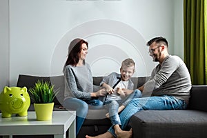 Happy parents and son having fun, tickling sitting together on the sofa, cheerful couple laughing, playing a game with their son,