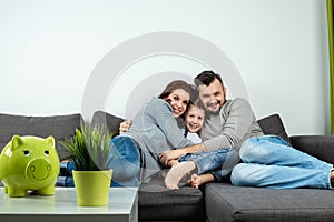 Happy parents and son having fun, tickling sitting together on the sofa, cheerful couple laughing, playing a game with their son,