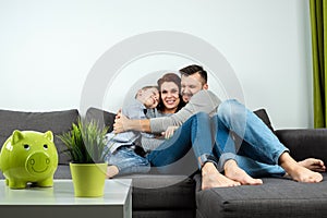 Happy parents and son having fun, tickling sitting together on the sofa, cheerful couple laughing, playing a game with their son,