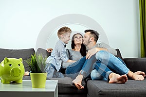 Happy parents and son having fun, tickling sitting together on the sofa, cheerful couple laughing, playing a game with their son,