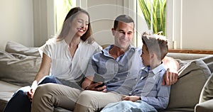 Happy parents talking joking to little son seated on sofa