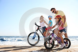 Happy parents teaching children to ride bicycles on sandy beach
