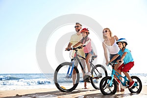 Happy parents teaching children to ride bicycles on sandy beach near sea