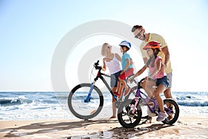 Happy parents teaching children to ride bicycles on sandy beach near sea