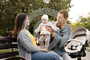 Happy parents with their adorable baby sitting on bench in park