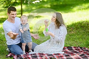 Happy parents and their child are having fun together outdoors, blowing bubbles. Smiling family with toddler enjoying