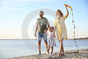 Happy parents with their child playing with kite on beach, space for text. Spending time in nature