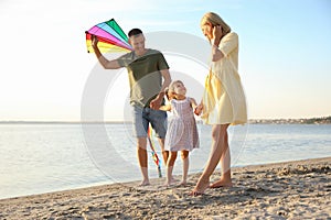 Happy parents with their child playing with kite on beach. Spending time in nature