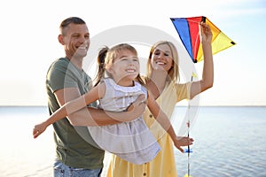 Happy parents with their child playing with kite on beach. Spending time in nature