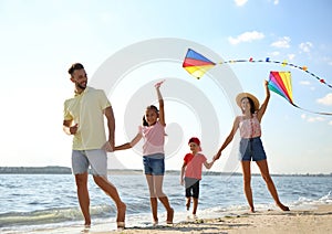 Happy parents and their children playing with kites on beach near sea. Spending time in nature