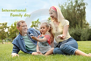 Happy parents and their daughter blowing soap bubbles in park on green grass. Happy Family Day