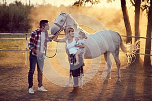 Happy parents with their daughter on the horse ranch.Young happy family having fun at countryside outdoors. Sunset, golden hour