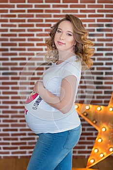 Happy parents-to-be couple looking at a cute red baby shoes for their unborn child, indoors studio portrait