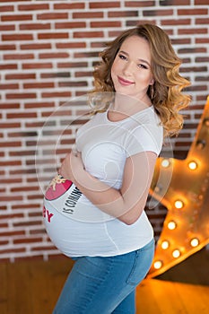 Happy parents-to-be couple looking at a cute red baby shoes for their unborn child, indoors studio portrait