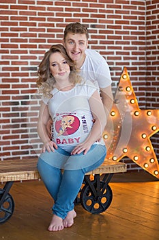 Happy parents-to-be couple looking at a cute red baby shoes for their unborn child, indoors studio portrait