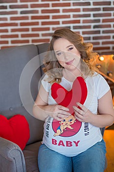 Happy parents-to-be couple looking at a cute red baby shoes for their unborn child, indoors studio portrait