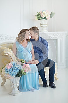 Happy parents-to-be couple looking at a cute red baby shoes for their unborn child, indoors studio portrait