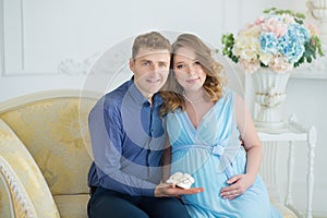 Happy parents-to-be couple looking at a cute red baby shoes for their unborn child, indoors studio portrait