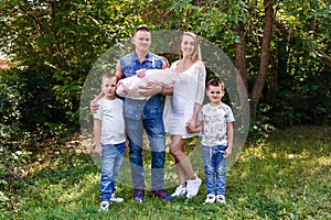 Happy parents and two children of preschoolers and newborn baby washed into the camera on a natural green background in the summer