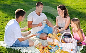 Happy parents with two kids having picnic together on green meadow in park