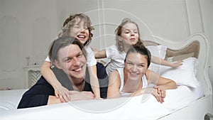 Happy Parents and Two Laughing Kids are Lying on the White Bed Having Fun Together During Weekend at Home. Young Couple