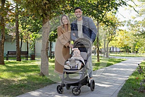 Happy parents walking with their baby in stroller at park on sunny day