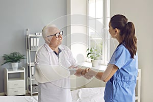 Happy patient with broken arm shaking hands with doctor, thanking for help and smiling