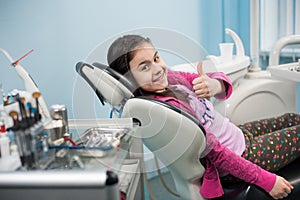 Happy patient girl showing thumbs up at dental clinic office. Medicine, stomatology and health care concept