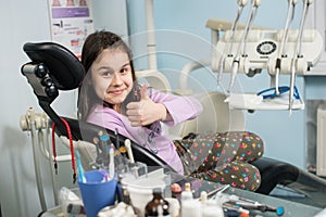 Happy patient girl showing thumbs up at dental clinic office. Medicine, stomatology and health care concept