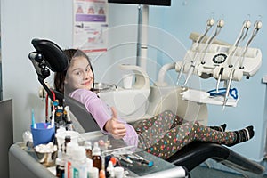 Happy patient girl showing thumbs up at dental clinic office. Medicine, stomatology and health care concept