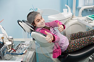 Happy patient girl showing thumbs up at dental office. Medicine, stomatology and health care concept