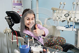 Happy patient girl showing thumbs up at dental office. Medicine, stomatology and health care concept