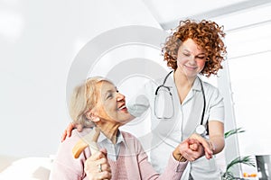 Happy patient is holding caregiver for a hand while spending time together. Elderly woman in nursing home and nurse. Aged elegant