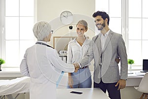 Happy young couple shaking hands with their family doctor or pregnancy specialist