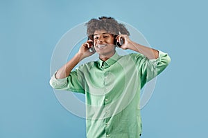 Happy peaceful african american guy listening to music in wireless headset, closing eyes and relaxing, blue background