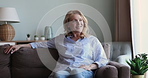 Happy peaceful older female homeowner dreaming relaxing on comfy couch