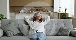 Happy peaceful woman relaxing on comfortable sofa in living room
