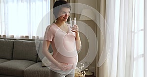 Happy peaceful young pregnant woman drinking glass of water.