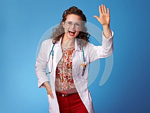 Happy pediatrist woman in white medical robe on blue greeting photo
