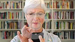 Happy pensioner browsing ebook reader application. Senior librarian with a phone smiling in a library or bookstore