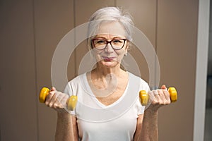 Happy pensioner exercising with dumbbells to maintain health