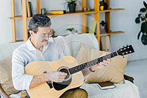 Happy pensioner in glasses playing acoustic guitar